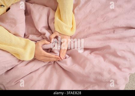 Self-love and well-being concept, woman making heart shape with hands on cozy pink bedding, top view Stock Photo