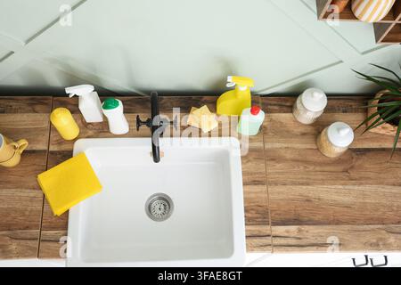 Home cleaning and kitchen hygiene concept, overhead view of sink with cleaning supplies and sponges on wooden countertop Stock Photo