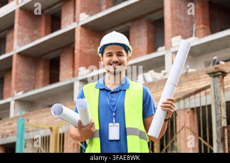 Construction project management and engineering, smiling male architect or builder holding blueprints at a building site Stock Photo