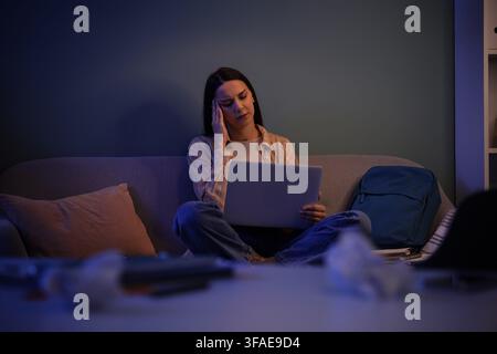 Burnout and remote work stress, young woman with headache working late on laptop at home in dark room Stock Photo