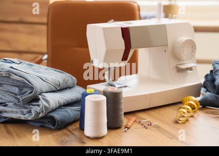 Fashion design and textile industry sewing machine with denim jeans thread spools and tailoring tools on a wooden table Stock Photo