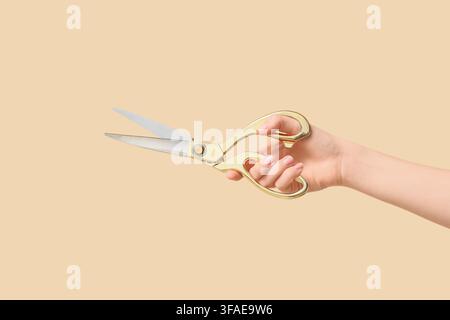 Crafting and tailoring concept womans hand holding golden scissors sewing and fashion design tools isolated on a beige background Stock Photo