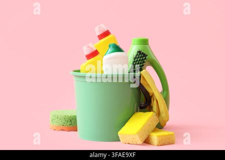 Home cleaning and household chores concept, bucket with various cleaning supplies and sponges on a pink background Stock Photo