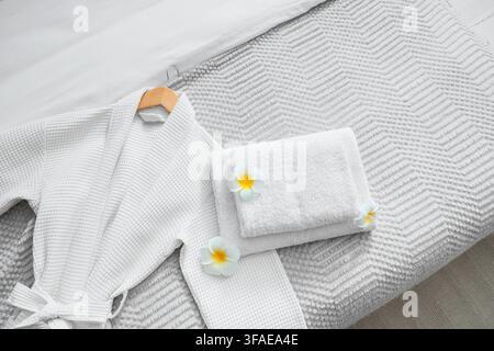 Clean towels with bathrobe and plumeria flowers on bed in hotel room, top view Stock Photo