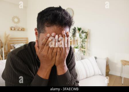 Man covering face with hands in indoor setting Stock Photo