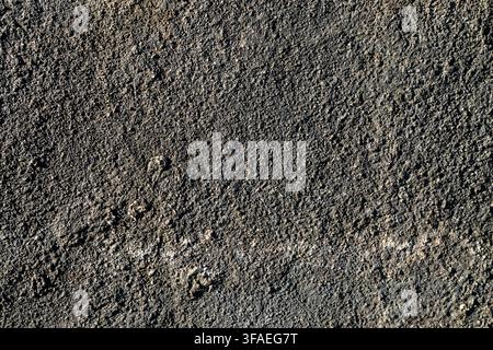 The texture of this asphalt surface is rough and dark, featuring small stone granules. It resembles rough, granular asphalt or concrete. Stock Photo