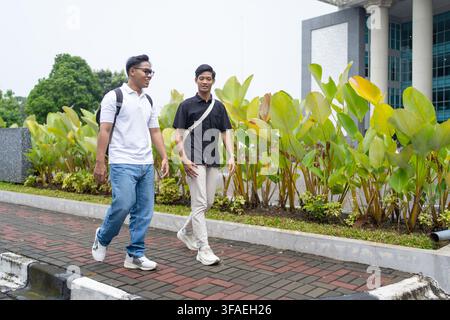 Two young Asian college students walking and talking together along a landscaped university campus walkway. Stock Photo