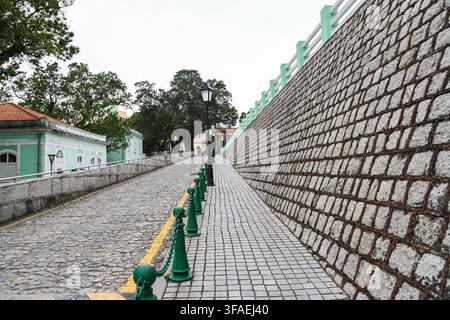 MACAU, CHINA, APRIL 2, 2026 Historic cobblestone street uphill road with massive stone brick retaining wall at Taipa district old town area Stock Photo