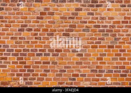 A close-up view of a textured brick wall. The wall features a mix of orange and brown bricks arranged in a uniform pattern Stock Photo