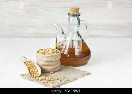 Corn oil in glass pitcher and dried corn kernels on white wooden background Stock Photo