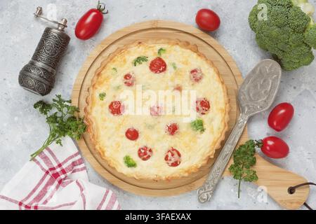 Quiche pie with broccoli, cherry tomatoes, salmon fish, cheese, eggs with cream on wooden cutting board and gray concrete background Stock Photo