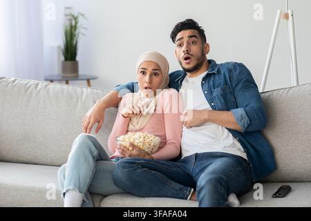 Shocked muslim couple watching thriller on TV Stock Photo