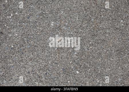 Full-frame close-up of a rough gray concrete surface with small exposed aggregate creating a neutral textured background. Stock Photo