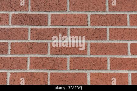 Close-up straight-on view of a red brick wall with gray mortar joints forming a repeating masonry pattern. Stock Photo