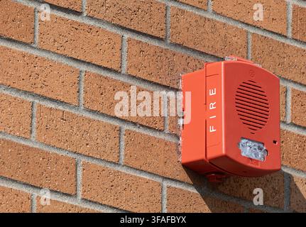Red fire alarm notification device mounted on an exterior brick wall with open space for text. Stock Photo