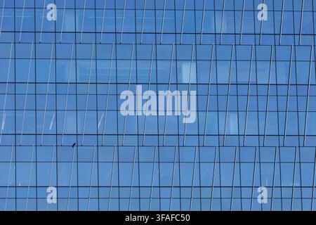Geometric facade of a modern office building with repeating blue windows and a small bird perched on the exterior. Stock Photo