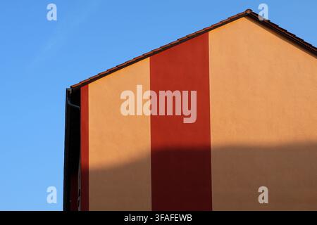 Minimalist architectural abstract of a building facade with yellow and red vertical stripes under blue sky Stock Photo