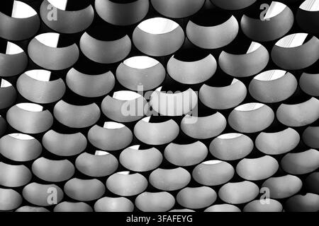 Abstract architectural pattern of curved metal panels with geometric holes and shadows in black and white Stock Photo