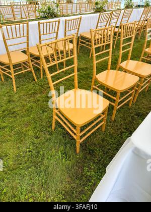 Riga, Latvia - August 1, 2026: Elegant gold Chiavari chairs arranged on a grassy lawn beside a white-draped banquet table, creating a refined setting Stock Photo