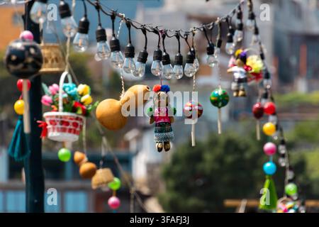 Colorful hanging ornaments and string lights in an outdoor market with blurred city background, showing handmade crafts, festive decor Stock Photo