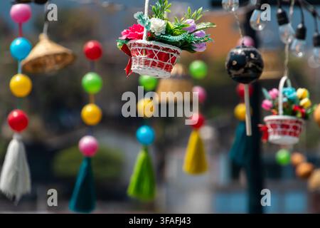 Colorful hanging ornaments and string lights in an outdoor market with blurred city background, showing handmade crafts, festive decor Stock Photo