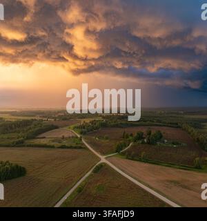 Aerial view of farmland, forests and rural roads beneath dramatic storm clouds illuminated by warm evening sunlight in Sigulda Municipality, Latvia. Stock Photo