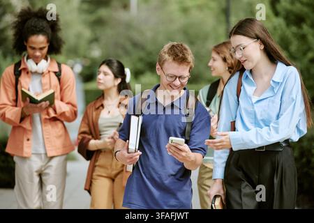 Diverse Students Walking on Campus and Looking at Smartphone Stock Photo