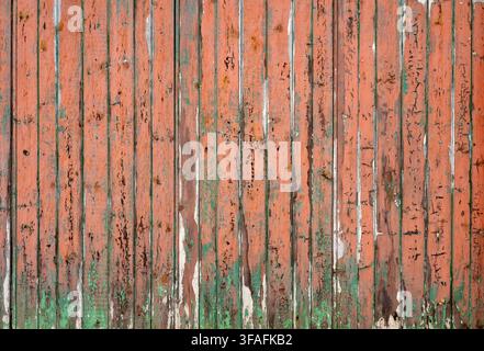 Weathered wooden weatherboarding in Lavenham, Suffolk, with faded orange paint peeling to reveal green undercoat, showing the rustic character of this Stock Photo