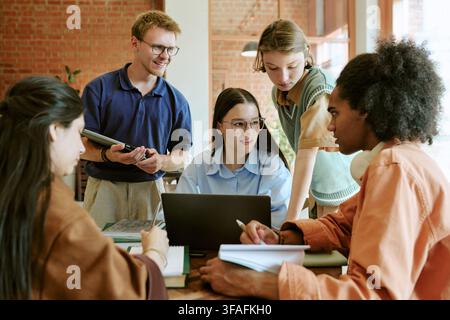 Diverse Students Collaborating on Group Project with Laptop in Campus Cafe Stock Photo