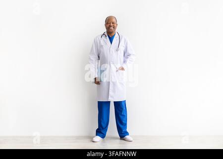 Full length of smiling mature Black doctor wearing white coat holding clipboard Stock Photo