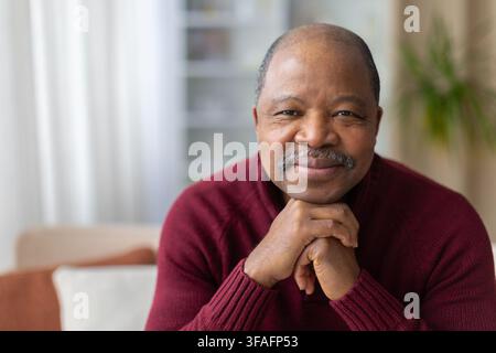 Closeup of thoughtful mature black man resting chin on hands, gentle smile Stock Photo