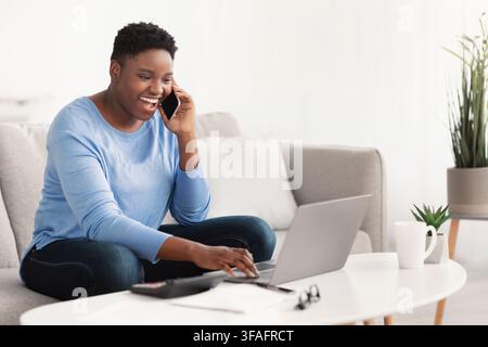 Black lady using laptop calling her friend, sitting on couch Stock Photo