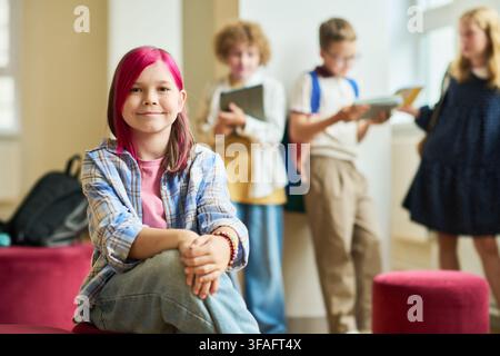 Portrait of Smiling Schoolgirl Sitting in Hallway with Classmates Stock Photo