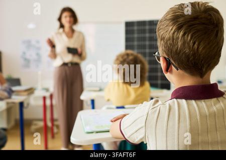 Schoolboy Listening to Female Teacher during Lesson in Classroom Stock Photo