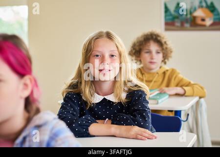 Portrait of Smiling Schoolgirl Sitting at Desk in Classroom Stock Photo