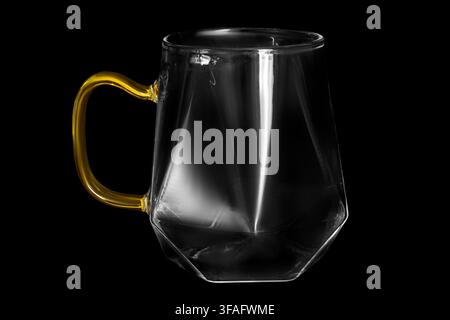 Clean glass mug with yellow handle isolated on black background Stock Photo