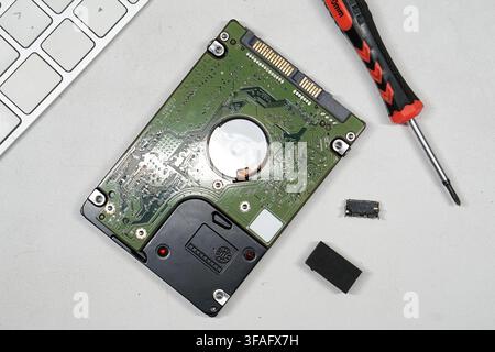 A top-down view showing a disassembled hard drive circuit board and a screwdriver, representing computer maintenance, hardware repair, and data recove Stock Photo