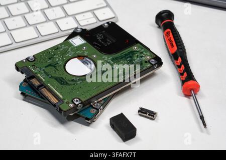 Close-up of disassembled hard disk drive with repair tools on white workspace for data restoration and hardware maintenance. Stock Photo