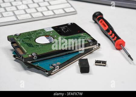 Close-up of disassembled laptop hard drives and a precision screwdriver on a white desk. Ideal for tech support, data storage maintenance, and hardwar Stock Photo