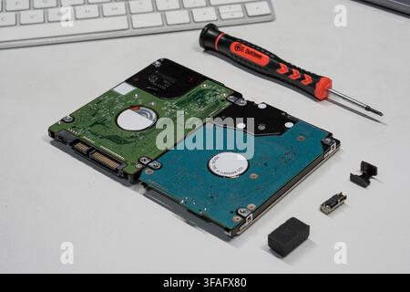 A high-angle view of two hard disk drives with exposed circuit boards and a repair tool on a white surface, focusing on computer hardware service. Stock Photo