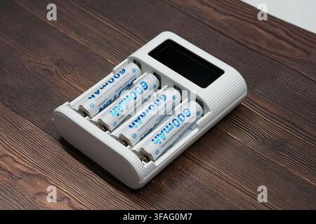 High-angle view of a white electronic charger with four 600mAh AAA rechargeable batteries on a dark wooden background. Concept for sustainable energy Stock Photo