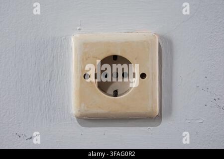 Close-up of aged, discolored white electrical socket on a textured wall. Focus on home maintenance and domestic energy. Stock Photo