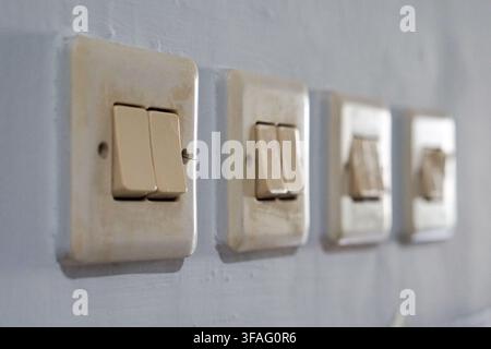 Row of used, vintage light switches on a grey wall. Focus on the aged plastic texture and electrical components of a domestic interior. Stock Photo
