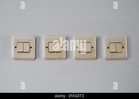 Row of four vintage yellowed double light switches on a light wall. Classic home electrical hardware for renovation and utility themes. Stock Photo