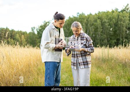 Agricultural analysts stand together studying data on tablet with focused expressions in wheat field. Concept of thorough agricultural analysis and co Stock Photo