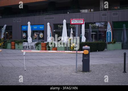 Automatic parking barrier gate and Droga Pożarowa sign in front of Pietro restaurant outdoor patio with umbrellas on ground floor of modern building. Stock Photo