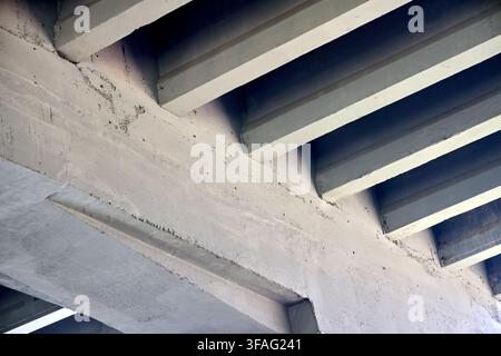 Concrete bridge underside featuring repeating diagonal beams, solid architectural structures, industrial infrastructure support, grey cement perspecti Stock Photo
