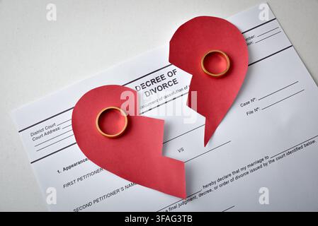 A red broken heart and two gold wedding rings sit on divorce papers, creating a strong visual metaphor for marital separation, loss and emotional pain Stock Photo