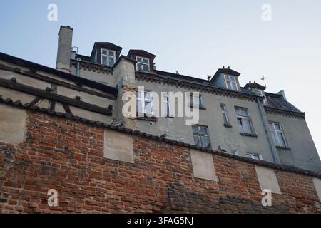Pigeons perch on the weathered, ancient red-brick defensive walls, with the crumbling plaster facade and dormer windows of an old residential building Stock Photo
