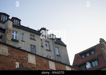 Pigeons perch on the weathered, ancient red-brick defensive walls, with the crumbling plaster facade and dormer windows of an old residential building. Stock Photo